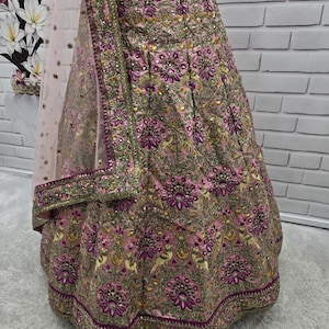May include: A pink and gold embroidered lehenga skirt with intricate floral and bird patterns. The skirt features a detailed border and is paired with a matching dupatta. The fabric has a shimmering effect, and the design is rich with embellishments.