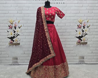 May include: A striking red lehenga, featuring detailed gold embroidery on the skirt and bodice. It includes a matching maroon dupatta with delicate detailing. The background displays the text "ANUGRAH OUTFIT".