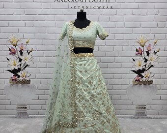 Op de afbeelding: Een mintgroene etnische outfit, weergegeven op een mannequin, met een top met korte mouwen en een lange rok. De outfit is versierd met ingewikkelde gouden borduursels en versieringen. De outfit is van Anugrah Outfit.