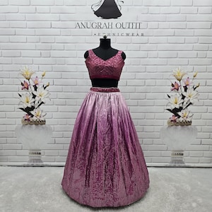 May include: A two-piece formal outfit on a mannequin. The top is a deep pink, sequined crop top with a V-neck. The skirt is a long, ombre design, transitioning from light pink to deep pink. The outfit is displayed in front of a white brick wall.
