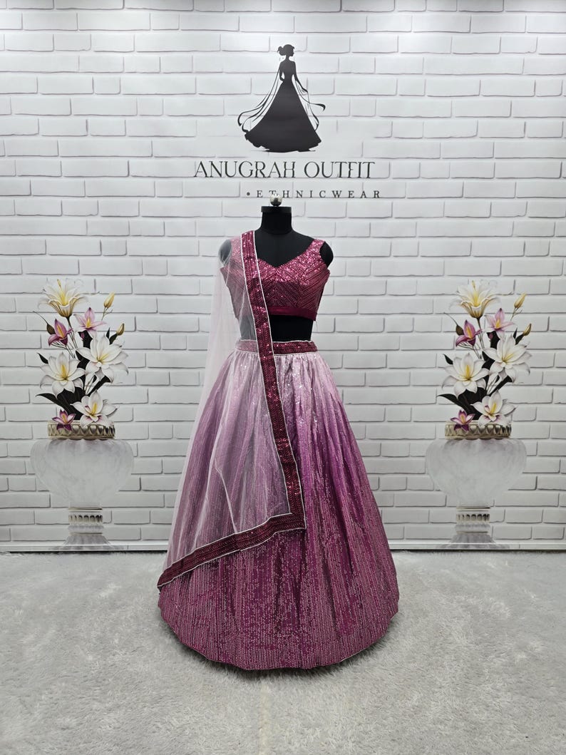May include: A formal magenta and pink sequined lehenga choli set on a mannequin. The set includes a sequined top, skirt, and a sheer dupatta with a magenta border. The background features a white brick wall with the text "ANUGRAH OUTFIT - ETHNICWEAR".