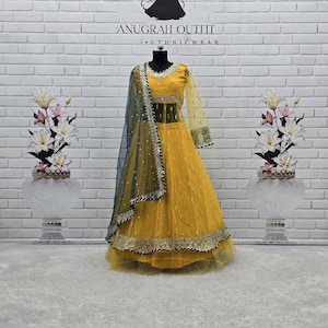 May include: A yellow lehenga choli set featuring a long-sleeved blouse and a full-length skirt with intricate gold embroidery and sequin detailing. A dark teal dupatta with a decorative border and scattered sequins is draped over the shoulder.