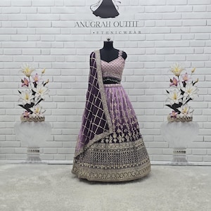 May include: A formal, two-piece outfit on a mannequin. The outfit features a lavender and purple skirt with intricate gold embroidery. The top is a matching lavender colour with a beaded design. A dark purple shawl with gold trim is draped over the shoulder. The text "ANUGRAH OUTFIT" is visible.