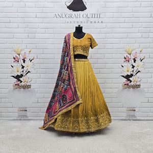 May include: A mustard yellow lehenga choli set featuring a short-sleeved blouse and a pleated skirt with intricate gold embroidery and mirror work. A multicoloured dupatta with a dark patterned border is draped over the shoulder of the mannequin.
