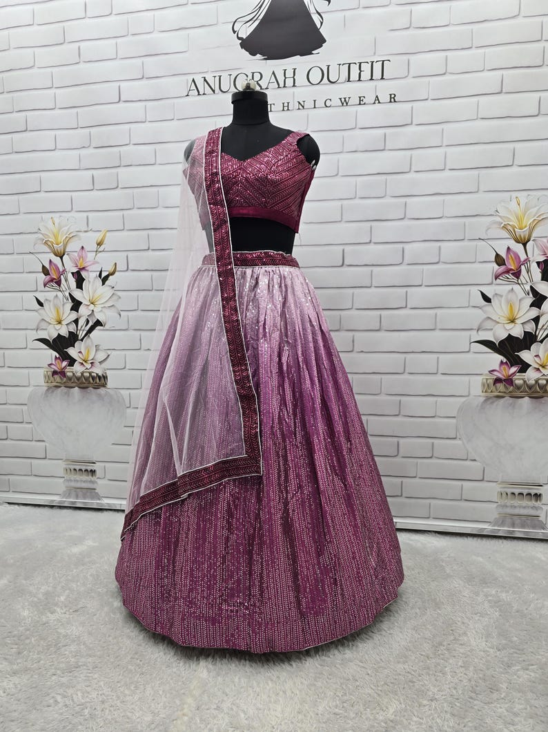 May include: A formal, two-piece outfit in shades of pink and purple, displayed on a mannequin. The top is a deep magenta, and the skirt transitions from light pink to a darker purple. A sheer, light pink scarf with a magenta border completes the ensemble. The outfit is labeled "ANUGRAH OUTFIT".
