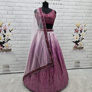 May include: A formal, two-piece outfit on a mannequin. The ensemble features a sequined, magenta-colored skirt that fades to a lighter shade of pink. The matching top is a deep magenta with a V-neck. A sheer, light pink scarf with a magenta border completes the look.