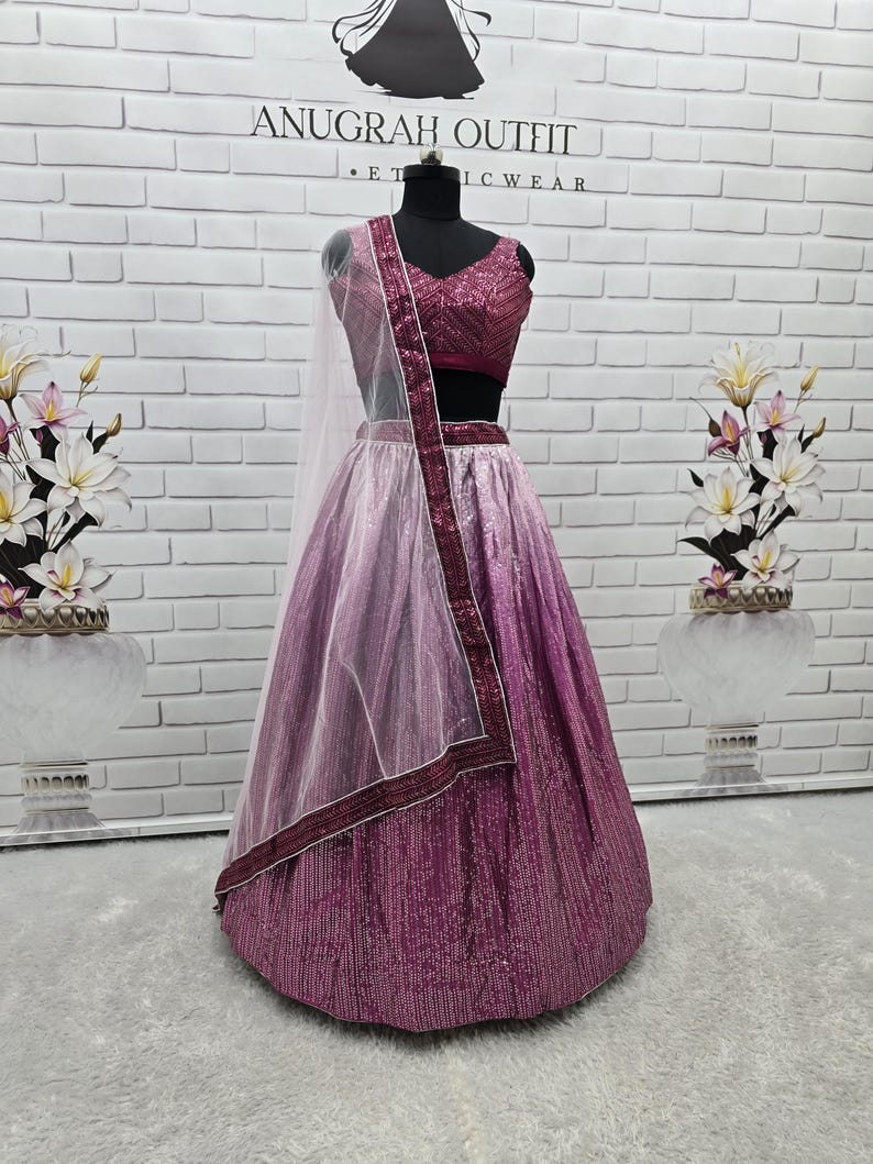 May include: A formal, two-piece outfit on a mannequin. The ensemble features a sequined, magenta-colored skirt that fades to a lighter shade of pink. The matching top is a deep magenta with a V-neck. A sheer, light pink scarf with a magenta border completes the look.