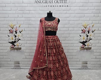 May include: A maroon and gold ethnic outfit, displayed on a mannequin. The outfit includes a heavily embroidered top, a patterned skirt, and a sheer dupatta. The text "ANUGRAH OUTFIT - ETHNIC WEAR" is visible above the outfit.