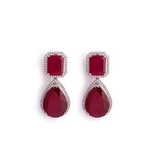 May include: A pair of drop earrings with a rectangular ruby at the top and a pear-shaped ruby at the bottom. Each ruby is framed by a halo of small, sparkling white stones. The earrings are set against a white background.