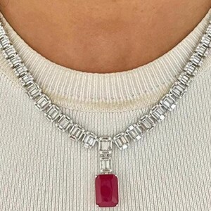 Puede incluir: Un collar de diamantes con un gran colgante de rubí rectangular. El collar presenta una serie de diamantes de talla rectangular engastados en una cadena de plata u oro blanco. El rubí es de color rojo intenso.