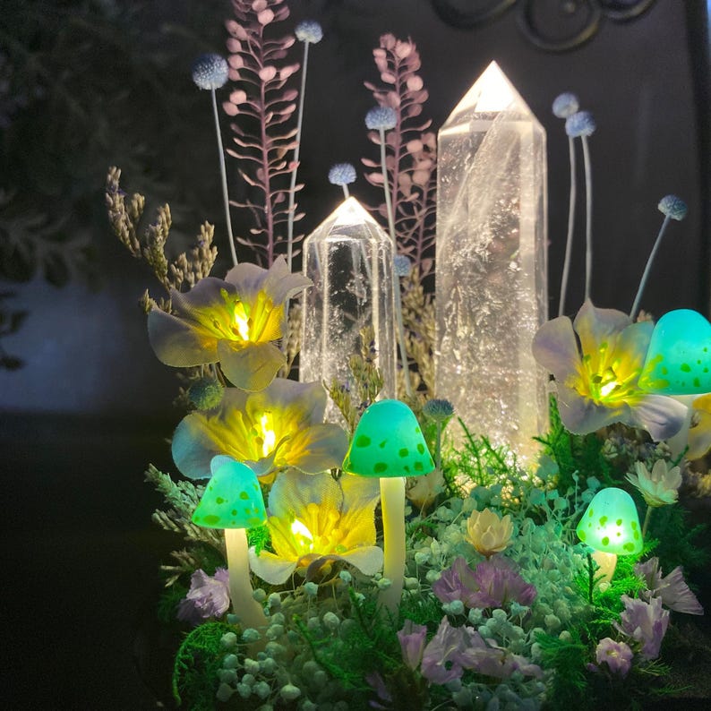 Pu&ograve; includere: Una composizione stravagante con funghi artificiali illuminati con cappucci verdi e steli bianchi, circondati da fiori gialli luminosi e punte di cristallo trasparente. La composizione include accenti floreali viola e rosa, creando un'estetica da favola.