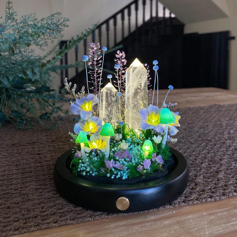 Pu&ograve; includere: Un'esposizione decorativa illuminata con tre punte di cristallo trasparente, fiori blu e gialli e funghi verdi luminosi. La composizione &egrave; inserita in una base nera e rotonda con un bottone color oro. I cristalli sono illuminati dall'interno.
