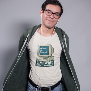 Op de afbeelding: Een crèmekleurig t-shirt met een afbeelding van een vintage computermonitor met de tekst 'An error has occurred.' Onder de monitor staat de tekst 'LIMEWIRE LOYALTY PROGRAM' gedrukt in een donkergroen rechthoekig kader.