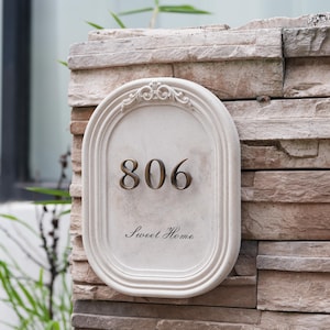 Puede incluir: Placa de dirección ovalada color crema con el número "806" en números color bronce. Las palabras "Sweet Home" están escritas en cursiva debajo. La placa está montada en una pared de piedra.