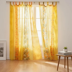 May include: Yellow sheer curtains with floral and patterned accents. The curtains hang from a silver rod, framing a window. The design includes a floral pattern and a patterned border in shades of orange and yellow.