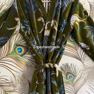 May include: Olive green velvet robe with a jungle print featuring leopards, palm trees, and zebra stripes. The robe has a matching tie belt and is hanging on a wooden hanger. The text "Zoopeyhandmade" is visible.