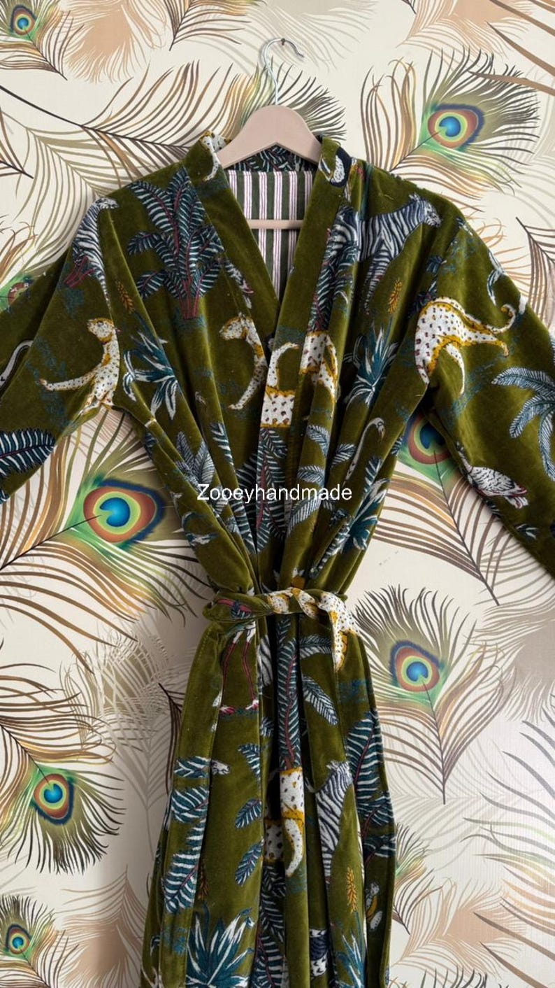 May include: Olive green velvet robe with a jungle print featuring leopards, palm trees, and zebra stripes. The robe has a matching tie belt and is hanging on a wooden hanger. The text "Zoopeyhandmade" is visible.