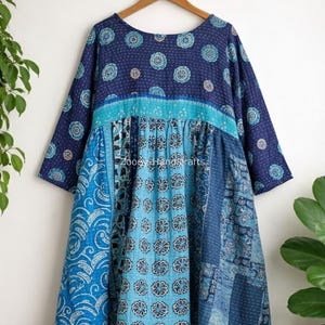 May include: A patchwork tunic dress in shades of blue, featuring a round neckline and three-quarter sleeves. The dress is adorned with floral and paisley patterns, with the text "Zooey Handcrafts" visible on the front.
