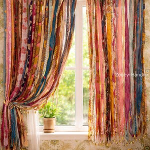 Könnte beinhalten: Bunte Fenstergardinen im Bohème-Stil aus vertikalen Stoffstreifen mit Mustern in Rosa, Gelb, Blau und Orange. Die Vorhänge sind mit goldfarbenem Seil und Quasten gebunden. Eine kleine Topfpflanze steht auf der Fensterbank.