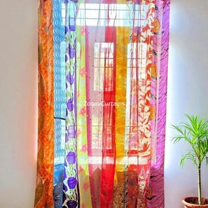 Può includere: Tende patchwork colorate appese davanti a una finestra. Le tende sono realizzate con vari tessuti nei toni dell'arancione, rosso, blu, viola e giallo. Il testo "ZooeyCurtains" è visibile sulle tende.