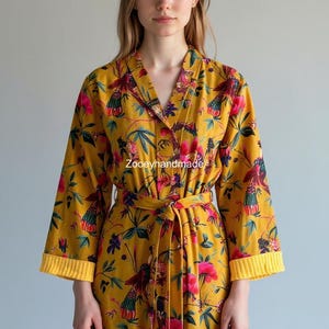 May include: A yellow floral robe with a V-neck and a matching belt. The robe features a vibrant pattern of pink and green flowers and birds. The sleeves have yellow cuffs. The text "Zooeyhandmade" is visible on the robe.