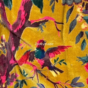 May include: Mustard yellow fabric with a vibrant floral and bird pattern. The design features colorful birds with red, blue, and green feathers, set against a backdrop of leaves and branches in shades of pink, green, and burgundy. The text "Zooeymade" is visible.
