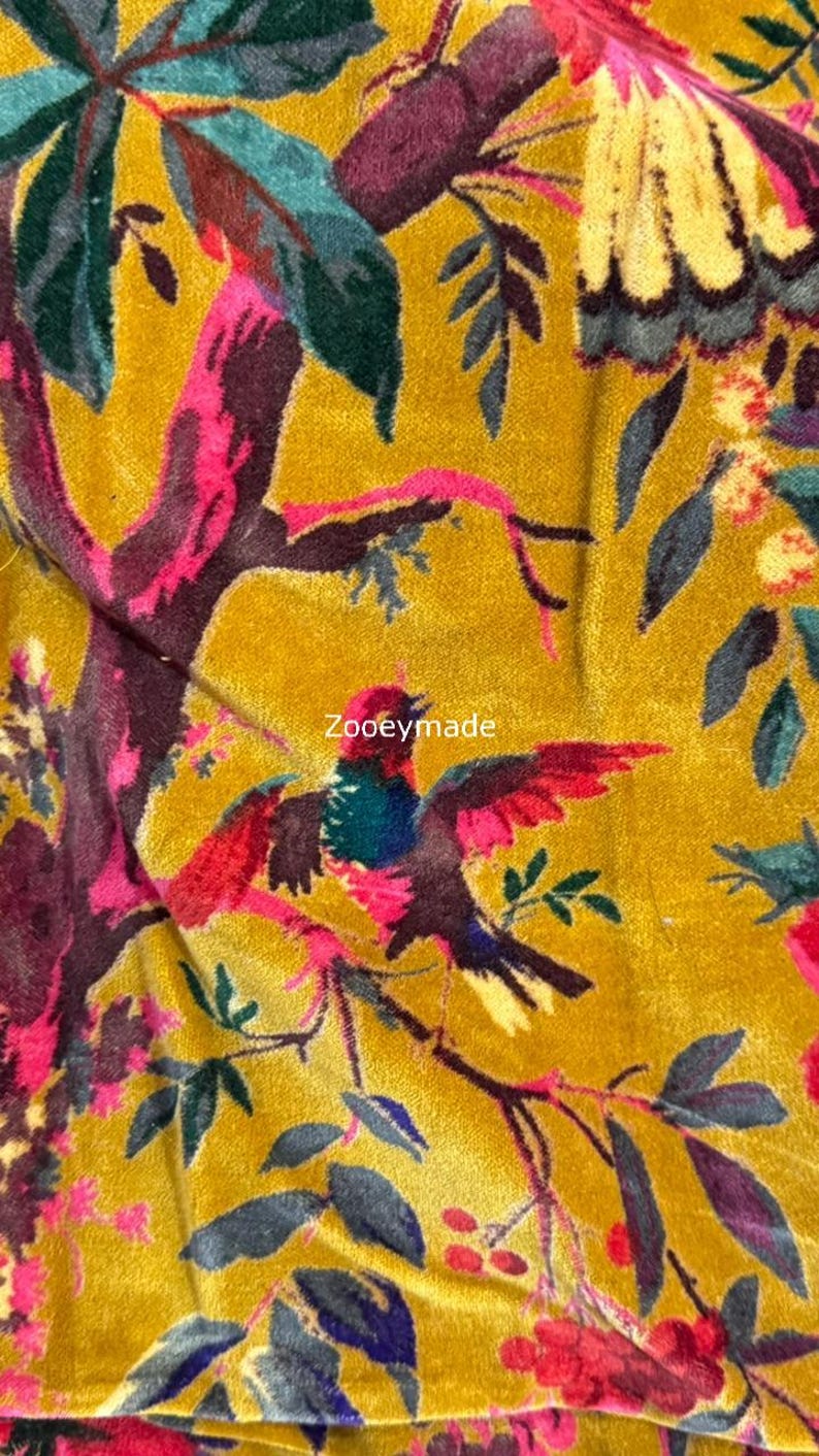 May include: Mustard yellow fabric with a vibrant floral and bird pattern. The design features colorful birds with red, blue, and green feathers, set against a backdrop of leaves and branches in shades of pink, green, and burgundy. The text "Zooeymade" is visible.