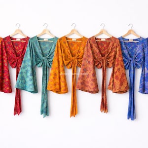 Può includere: Una collezione di top avvolgenti colorati e fantasia, nelle tonalità dell'arancione, del rosso, del verde acqua e del blu. Ogni top ha maniche lunghe a campana e una chiusura con fiocco in vita. I top sono appesi a grucce di legno.
