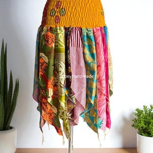 Könnte beinhalten: Bunter Patchwork-Rock mit gelbem Gummibund. Der Rock hat florale und gemusterte Stoffe in Grün, Rosa und Orange. Der Rock wird auf einer Schaufensterpuppe präsentiert. Einzigartiges Kleidungsstück.