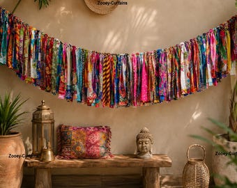 May include: A long, decorative garland made of numerous hanging fabric strips in a wide variety of vibrant colors and diverse patterns. The strips are tied together in a horizontal row, creating a dense, multi-colored fringe effect across the wall.
