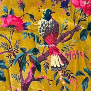 May include: Mustard yellow fabric with a floral and bird design. The fabric features a bird with a red tail and a black and white spotted back, perched on a branch. Pink flowers and teal leaves are also present.