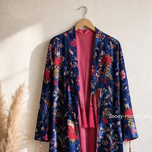 May include: A blue floral patterned kimono-style robe with a pink interior, hanging on a wooden hanger. The robe features red and pink floral designs. The text "Zooey-Handicrafts" is visible on the lower right side of the robe.