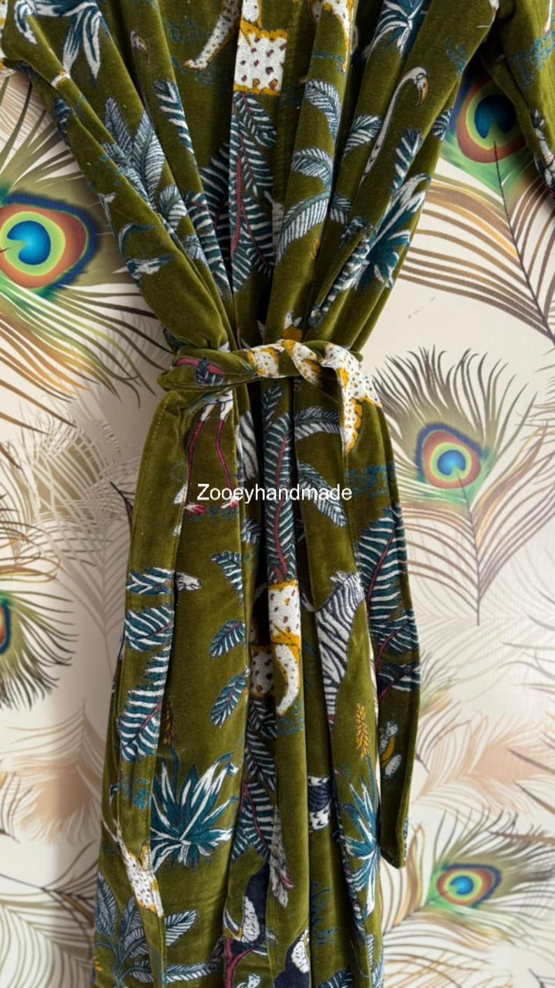 May include: Olive green velvet robe with a jungle print featuring white and yellow animal figures, blue and white leaves, and the text "Zooeyhandmade". The robe is tied with a matching belt.