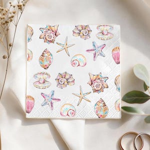 May include: Square white paper napkin with a repeating pattern of watercolor seashells and starfish in pastel colors. The napkin features a textured, diamond-shaped pattern.