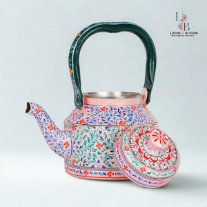 Può includere: Una teiera rosa e argento dipinta a mano con coperchio abbinato. La teiera presenta un manico verde ed è adornata da intricati motivi floreali blu, rossi e verdi. È un oggetto decorativo.