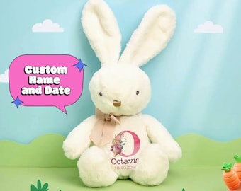 May include: A cream-colored plush rabbit toy with long ears and a tan ribbon tied around its neck. The rabbit features a printed design on its chest showing a large letter O, a small rabbit illustration, the name Octavia, and the date 12.10.2024.