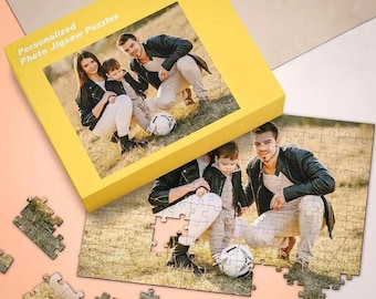 Peut inclure: Une boîte jaune pour un puzzle photo personnalisé présentant l'image imprimée d'une famille avec un enfant et un ballon de football. À côté de la boîte se trouve un puzzle partiellement assemblé affichant la même photo sur un terrain herbeux.