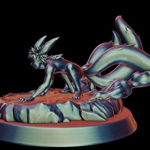Può includere: Statuetta dettagliata di un personaggio con orecchie da volpe e code multiple, in posizione accovacciata. La figura è principalmente blu e verde, con una base marrone-rossastra e uno sfondo nero. La scultura è alta circa 15 cm.