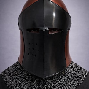 May include: A medieval knight's helmet with a black visor and a copper-colored top. The helmet has a series of small holes on the visor and is paired with a chainmail collar. The background is a solid, light purple color.