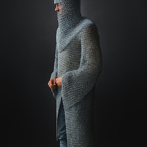 May include: A full-length, chainmail garment, including a hood, worn over blue jeans. The metallic armor is a silvery-gray color and covers the entire upper body and head. The person is standing in profile against a dark background.
