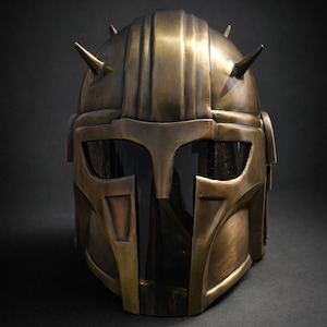 K&ouml;nnte beinhalten: Ein bronzefarbener Helm mit dunklem Visier und spitzen H&ouml;rnern. Der Helm hat eine detaillierte, metallische Oberfl&auml;che und ein Design, das an eine Kriegerr&uuml;stung erinnert. Die Gesamt&auml;sthetik deutet auf ein futuristisches oder Fantasy-Thema hin.