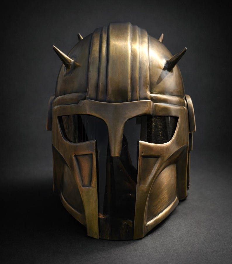 K&ouml;nnte beinhalten: Ein bronzefarbener Helm mit dunklem Visier und spitzen H&ouml;rnern. Der Helm hat eine detaillierte, metallische Oberfl&auml;che und ein Design, das an eine Kriegerr&uuml;stung erinnert. Die Gesamt&auml;sthetik deutet auf ein futuristisches oder Fantasy-Thema hin.