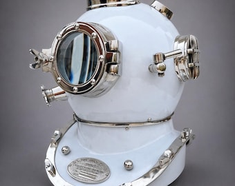 May include: A white diving helmet with polished silver accents. The helmet features a large, circular viewing window and various metallic fixtures. The base has a decorative silver trim and a small, oval plaque. The helmet is a vintage nautical item.