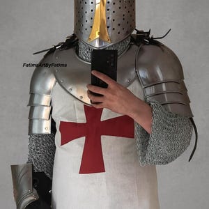 May include: A suit of medieval armor, including a helmet, chainmail, and metal plating. The helmet has a gold accent. A white tunic with a large red cross is visible. The image includes the text "FatimaArtByFatima".