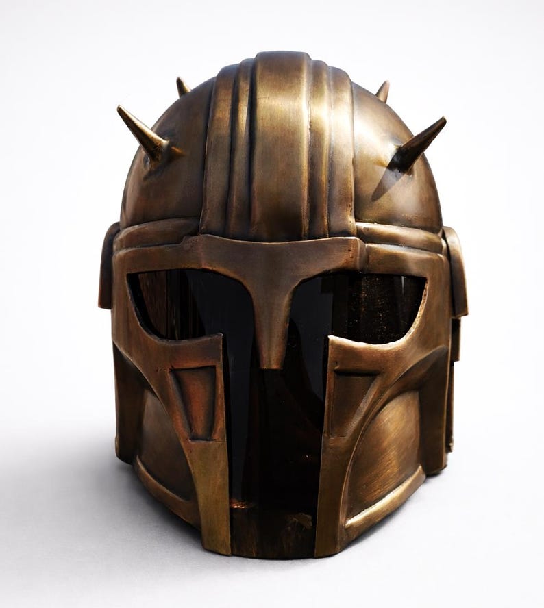 K&ouml;nnte beinhalten: Ein bronzefarbener Helm mit detailliertem Design, mit Visier und mehreren spitzen Stacheln. Der Helm hat ein verwittertes Aussehen, das auf eine kampferprobte &Auml;sthetik hindeutet. Das Gesamtdesign erinnert an einen Kriegerhelm.