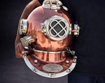 Pode incluir: Um capacete de mergulho de cobre vintage com detalhes prateados. O capacete tem formato redondo com uma grande janela frontal e vários óculos. O cobre tem um acabamento polido, que reflete a luz. Uma peça clássica para decoração náutica.