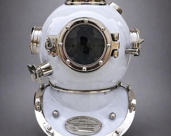 Op de afbeelding: Witte duikhelm met een rond glazen vizier en metalen accenten. De helm heeft een afgeronde bovenkant, zijbevestigingen en een decoratieve metalen plaat aan de voorkant. Het ontwerp doet denken aan antieke maritieme apparatuur.