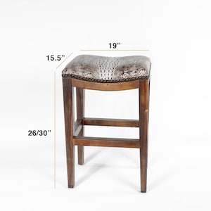 Pode incluir: Banqueta de bar de madeira com assento em pele de cobra sint&eacute;tica. O assento mede 48 cm de largura e 39 cm de profundidade. A altura da banqueta &eacute; de 66/76 cm. A estrutura &eacute; de madeira castanha escura.