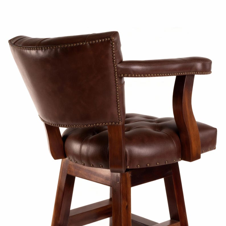 May include: A brown leather bar stool with a tufted seat and backrest. The chair has wooden armrests and a wooden frame. The leather is a rich, dark brown color, and the chair is accented with brass-colored nailhead trim.