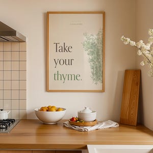 Könnte beinhalten: Kücheninterieur mit einer Holz-Arbeitsplatte, einem gerahmten Druck mit dem Text "Take your thyme" und einer Schüssel mit Orangen. Ein Holzschneidebrett und eine Vase mit weißen Blumen sind ebenfalls vorhanden.